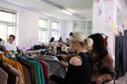 Stojany se secondhand oblečením, které se prohlížejí lidé ve velké světlé místnosti