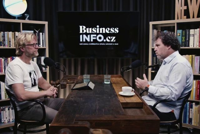 Moderátor Martin Zika a host Václav Muchna sedí naproti sobě u velkého dřevěného stolu. V pozadí mezi nimi velká černá obrazovka s logem BusinessInfo.cz a z každé strany je knihovna.